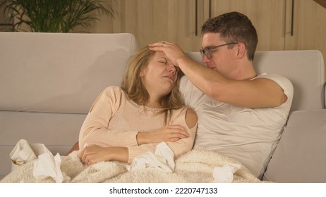 CLOSE UP: Couple On Cosy Sofa Watching TV While Lady With Headache Is Being Sick. Winter Colds And Viruses Spreading Around. Married Couple Sitting On Comfy Couch While Woman Is Having Seasonal Virus.