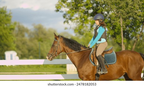 CLOSE UP: Courageous young girl horseback riding beautiful dark brown mare trotting in outdoors manege at horse ranch. Youngster rider exercising, learning and training at riding school - Powered by Shutterstock