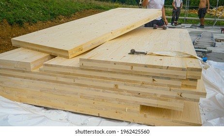 CLOSE UP: Cross-laminated timber wall panels lie on the ground next to a group of unrecognizable workers. A stack of CLT wall panels lie uncovered at a construction site of a modern housing project.