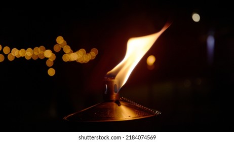 CLOSE UP: Detailed view of burning flame from metal oil lamp at night time. Orange glowing flame from oil based lamp with black background and bokeh. Mesmerizing ambiance light for evening mood.