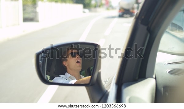 CLOSE UP, DOF: Angry Caucasian man throwing a temper\
tantrum while driving to work during rush hour. Furious young male\
driver shouting at the cars in front of him as he gets stuck in a\
traffic jam.