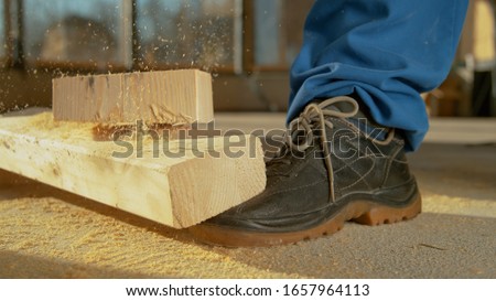 CLOSE UP, DOF: Detailed shot of a painful work accident as a heavy plank falls on an unrecognizable worker's foot. Worker sawing wood drops a beam on his foot. Unlucky construction site accident