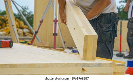 CLOSE UP, DOF: Unrecognizable male builder picks up a CLT beam from a workbench at an unfinished housing project. Contractor carries a glued laminated board across the bustling construction site - Shutterstock ID 1961969287