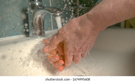 CLOSE UP, DOF: Unrecognizable Older Man Is Washing His Hands In The Bathroom To Get Rid Of Coronavirus Germs. Responsible Elderly Woman Washing Her Hands With Water During The COVID-19 Outbreak.