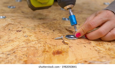 CLOSE UP, DOF: Unrecognizable Woman With Red Nails Fastens A Metal Washer Onto Plywood Board With A Power Drill. Close Up Shot Of A Female Worker Screwing Thin Metal Discs In Place On A Plywood Panel.