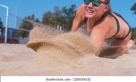 CLOSE UP, DOF: Young female athlete dives into the sand and saves a point during beach volleyball match. Cheerful Caucasian girl jumps and crashes into the white sand during a beach volley tournament. - Powered by Shutterstock