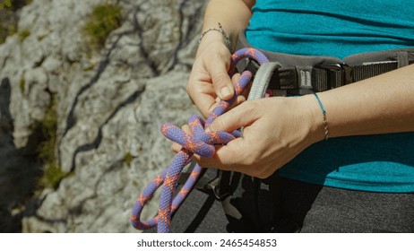 CLOSE UP, DOF: Young woman ties a belay rope around the waist harness before top rope climbing up a challenging cliff. Athletic female creates a knot after pulling safety rope through the harness. - Powered by Shutterstock