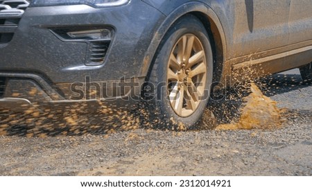 CLOSE UP: Driving car hits a pothole in asphalt road and splashes muddy rainwater. Dangerous driving on bumpy paved roads through the tropical rural landscape. Poor road maintenance in third world.