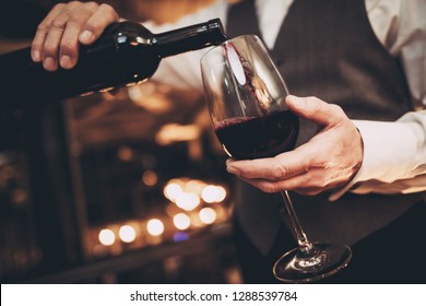 Close up. Elegant waiter pours red wine from bottle into glass at restaurant. Sommelier tasting wine in restaurant.