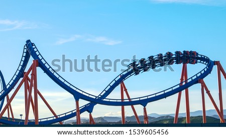 CLOSE UP: Excited tourists are thrown around as the ride the epic roller coaster speeding into a sharp turn. Thrill-seeking tourists ride the fun roller coasters in an amusement park in Los Angeles.