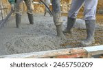 CLOSE UP: Fresh concrete flows out of a wide hose as contractors pour a reinforced slab at the ground floor of a house under construction. Unrecognizable builder is pouring a large concrete slab.