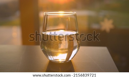 CLOSE UP: Fresh water in glass jar backlit with golden sunlight placed on table. Sun reflecting from drinking glass filled with water. Transparent and colourless fluid in a glass jar.