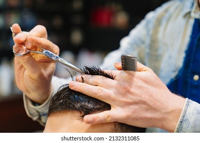 Close Up. The Hairdresser Makes A Haircut For A Brunette Man With A Scissors In A Barbershop. Professional Services. Beauty Salon For Men. Cosmetics And Products For Scalp And Hair Care.