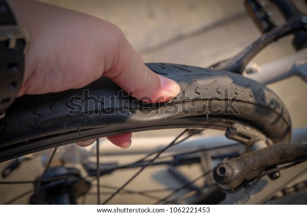 Close up: Hand touching flat tire of bicycle is\
on road in the morning