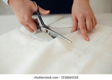 Close up. hands woman Tailor working cutting a roll of fabric on which she has marked out the pattern of the garment she is making with tailors chalk.