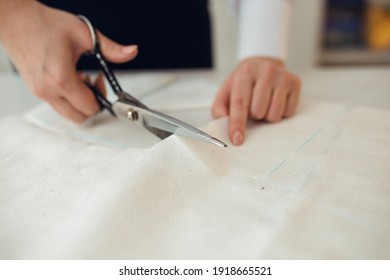 Close up. hands woman Tailor working cutting a roll of fabric on which she has marked out the pattern of the garment she is making with tailors chalk.