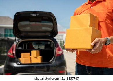 Close Up, Handsome Asian Delivery Man In An Orange Uniform Holds Box Of Products For Customers Online Order. Domestic And International Transport And Logistics. Delivery Service Dealer