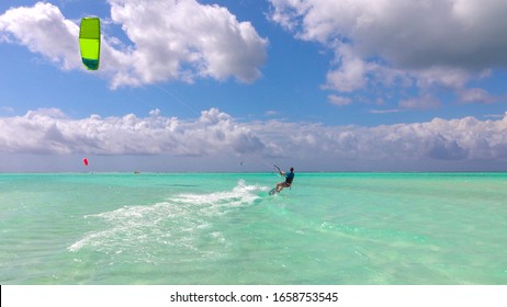 CLOSE UP: Happy young female kiter does a kitesurfing water start on perfect turquoise sea on sunny day. Cheerful kiteboarder woman kiting in beautiful blue lagoon in stunning Zanzibar kite spot