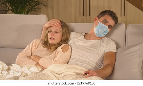 CLOSE UP: Husband Comforting His Coughing Sick Wife While She Is Having A Flu. Winter Colds And Viruses Spreading Around. Married Couple Cuddling On Comfy Couch While Woman Is Having Seasonal Virus.