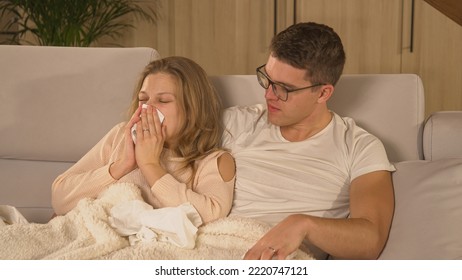 CLOSE UP: Husband Comforting His Coughing Sick Wife While She Is Having A Flu. Winter Colds And Viruses Spreading Around. Married Couple Cuddling On Comfy Couch While Woman Is Having Seasonal Virus.