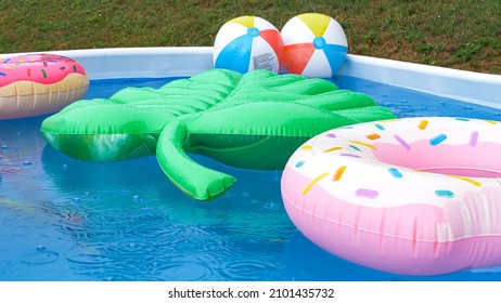 CLOSE UP: Inflatable Leaf, Donuts And Balls Float Around A Pool During A Late Summer Rainstorm. Colorful Floaties Are Floating Around The Empty Home Pool On A Rainy Afternoon In Someone's Backyard.