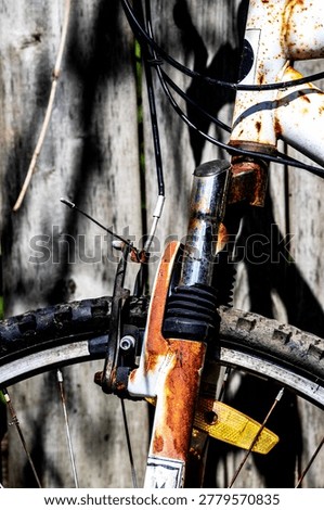Close up, isolated, front wheel of bike. Abandoned, forgotten, discarded bicycle. Rubber tire, wheel, spokes. Hand brake. Rusty, rusted, corroded. Leaning against weathered wooden fence. Light and shadow. 