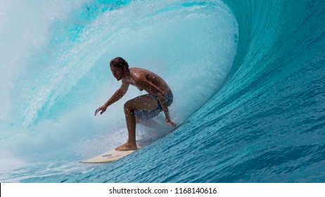 CLOSE UP: Large Tube Wave Curls Behind Fearless Sportsman Surfing Near A Famous Surf Spot In Tahiti. Focused Pro Surfer Rides A Big Emerald Wave. Crystal Clear Ocean Water Splashing High In The Air.