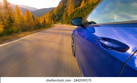 CLOSE UP, LENS FLARE: Brand New Sportscar Speeds Down An Empty Mountain Road In The Italian Alps At Sunset. Golden Fall Sunbeams Shine On A Shiny Blue Car Driving Along Scenic Route In The Dolomites.