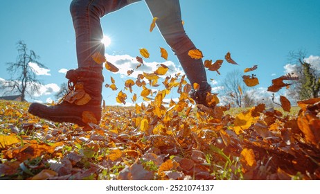 CLOSE UP, LENS FLARE: Female hiker wearing boots runs across a meadow full of beautiful fallen leaves. Unrecognizable woman having fun running in the sunlit rural landscape kicking up dry leaves. - Powered by Shutterstock