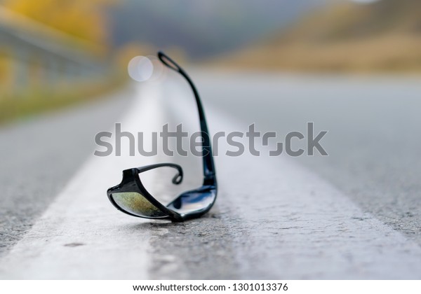 close up, lost sunglasses\
lie on the road asphalt on a country track on the dividing strip at\
the curb