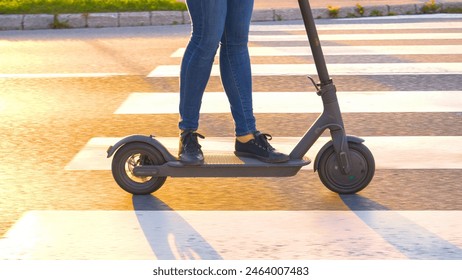 CLOSE UP, LOW ANGLE: Cinematic shot of modern girl's legs as she rides an e-scooter at sunset. Unrecognizable woman in jeans rides an electric scooter down an empty road on a sunny evening in autumn. - Powered by Shutterstock