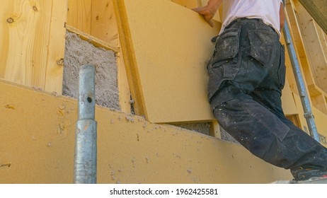 CLOSE UP, LOW ANGLE: Contractor Lays Insulation Panels On A Wall Filled With Blown Cellulose. Unrecognizable Builder Installs Thermal Insulation Sheets On The Modern Real Estate Housing Project.