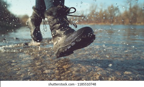 CLOSE UP, LOW ANGLE, DOF: Energetic Young Woman In Fuzzy Black Boots Playing By The Tranquil Stream On A Lovely Autumn Day. Unrecognizable Playful Hiker Girl Running And Splashing Pure River Water.