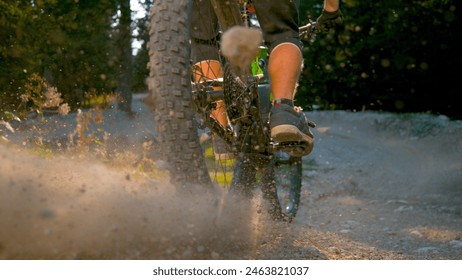 CLOSE UP, LOW ANGLE, DOF: Unrecognizable man on mountain bicycle kicks up dust while speeding downhill down a sunlit gravel track. Cool action shot of man riding an electric bike down dirt road. - Powered by Shutterstock