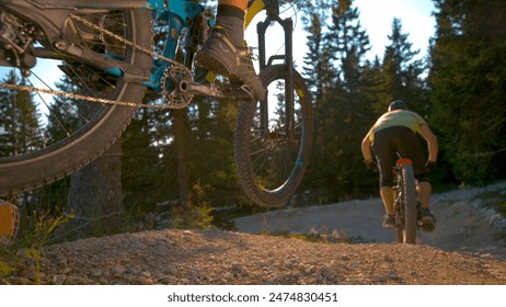 CLOSE UP, LOW ANGLE, DOF: Two extreme mountain bike riders speed along an empty gravel track in the green forest. Cool action shot of unrecognizable friends racing on high tech electric bicycles. - Powered by Shutterstock