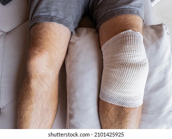 CLOSE UP: Male Patient's Knee In Home Care Is Wrapped In Bandages After A Meniscus Surgery. Detailed Shot Of A Man's Legs And His Bandaged Knee After Surgery. Man Is Recovering After Knee Surgery.