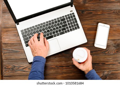 Close Up, Man Hands Holding Blank Screen Cell Phone, Disposable Paper Coffee Cup, Male Blogger Typing, Browsing, Surfing, Laptop Pc Computer, Wooden Table Background. Top View, Overhead, First Person.