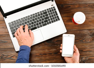 Close Up, Man Hands Holding Blank Screen Cell Phone, Disposable Paper Coffee Cup, Male Blogger Typing, Browsing, Surfing, Laptop Pc Computer, Wooden Table Background. Top View, Overhead, First Person.