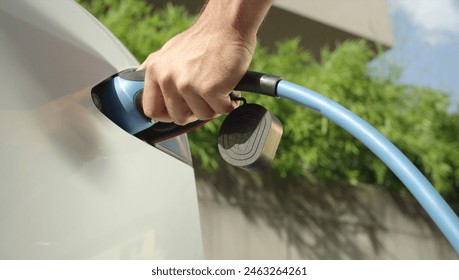 CLOSE UP: Man plugging in electric car at home at electro charging station. Luxury white electrical Tesla car recharging. Environmentally conscious man charging his electric vehicle - Powered by Shutterstock