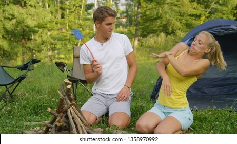 CLOSE UP: Man And Woman On An Outdoor Camping Adventure Wave Their Arms As They Get Swarmed By Pesky Mosquitoes. Young Tourist Couple Trying To Get Rid Of Annoying Insects Harassing Them In The Wild.