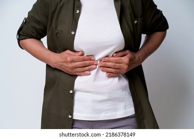 Close Up. Mature Woman Having Stomach Problems Experiencing Pain In Dark Green Shirt Isolated On White Background. No Face Visible Middle Aged Woman With Abdominal Pain. Healthcare Concept.