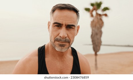 Close up, middle-aged muscular man looks at the camera while sitting on the promenade after jogging - Shutterstock ID 2308476859