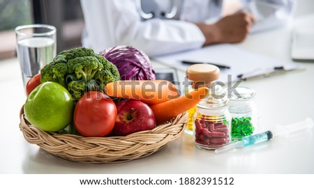 Close up, natural fresh fruits, apple, broccoli, carrot, vegetables and multivitamins in the basket on the table. Blurred background is a doctor or nutritionist advising about healthy lifestyles