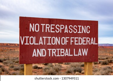 Close up. No trespassing - Violation of federal and tribal law - warning brown road sign with white lettering on the wooden post in desert landscape, overcast during day time. Close up