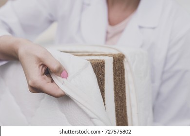 Close up. An orthopedic woman shows the man a sample of the mattress he wants to buy. A woman holds a pattern in her hands and shows what it's made of - Shutterstock ID 727575802