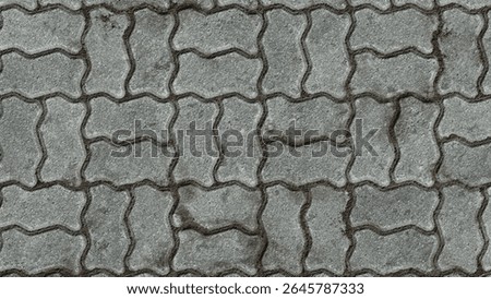 A close up, overhead shot of interlocking gray pavement bricks. The bricks create a repeating pattern, forming a durable and textured surface.