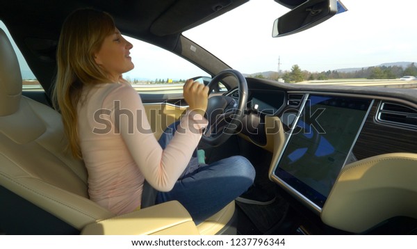 CLOSE UP: Playful young woman dancing and\
singing in her car driving itself down the freeway. Cheerful\
Caucasian female enjoying the music during a relaxing road trip to\
her vacation destination.