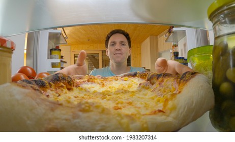 CLOSE UP, PORTRAIT: Smiling Caucasian Man On A Diet Gives Into The Temptation And Takes A Pizza Out Of His Fridge. Happy Guy Picks Up A Pizza Off The Top Shelf Of His Massive American Refrigerator.