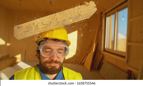 CLOSE UP, PORTRAIT: Wooden Board Falls On A Young Worker's Head. Small Plank Falls From Above On An Unsuspecting Contractor's Head. Protective Hard Hat Saves Caucasian Builder's From A Concussion.