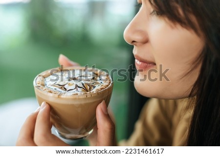 Close up, Portrait young beautiful woman with coffee latte art  in coffee shop, she holding and inhale aroma of coffee and admire the beauty of milk froth in coffee cup